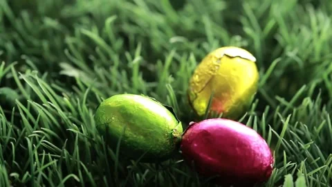 Camera shift initiating three foil-wrapped eggs rolling and rotating revealing Video stock 330033012