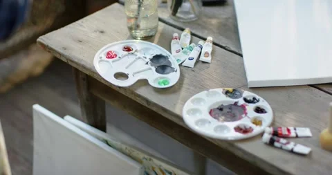 Camera is shifting right, revealing palettes, tubes, jar, canvas on bench, Stock Footage 340882307