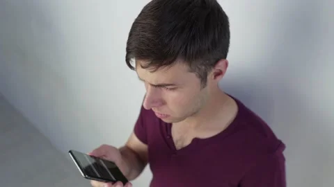 Camera shoots from the top upset young man looking at smartphone screen Stock Footage 208373538