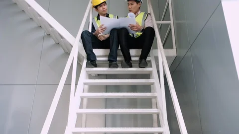 Camera shot tilt up,engineer and architect sit on stairs looking blueprint. Stock Footage 129584733