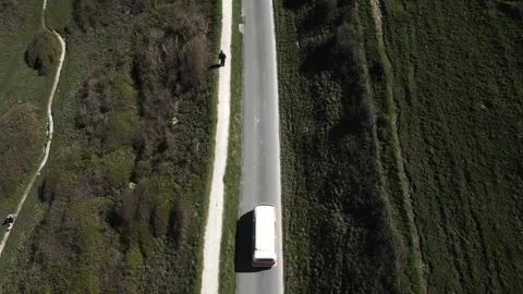 Camera shows van moving on narrow road then pans to expansive hilly landscape Stock Footage 247054729