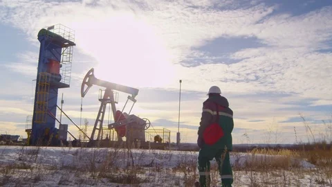 Camera Shows Worker Walking against Oil Well and Derrick Stock Footage 79477037