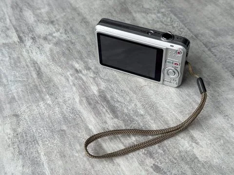 Camera sits on a wooden table with a strap on a gray surface 库存照片