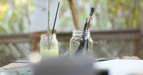 Camera is sliding and pulling focus, revealing two glass jars of brushes on Stock Footage 336438234
