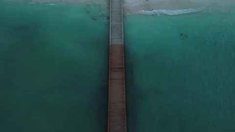 Camera smoothly ascends to capture perspective of pier, tourist beach and hotel Stock Footage 274068066