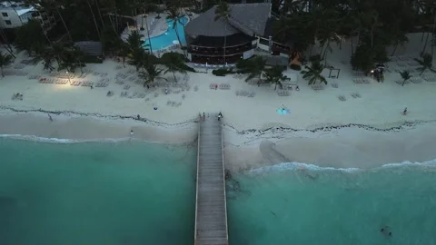Camera smoothly ascends to capture perspective of pier, tourist beach and hotel Stock Footage 274374974