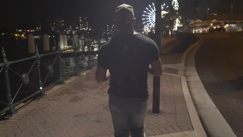 Camera Smoothly Follows Man Walking On Path Towards Theme Park at Night Stock Footage 107899264