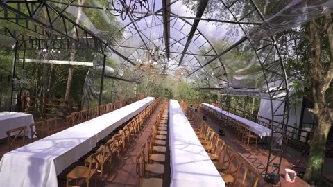 Camera spin effect over long wedding banquet tables in transparent ecolodge Stock Footage 325268730