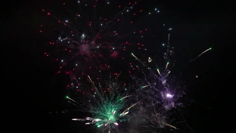 Camera tilt from mixed barrage of medium fireworks up to large slow fireworks Video stock 235014905