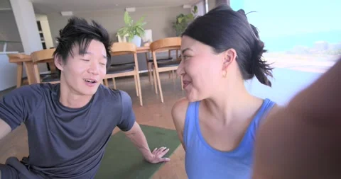 Camera tilting, couple sitting on green mat at home in workout gear, filming, Stock Footage 340393798