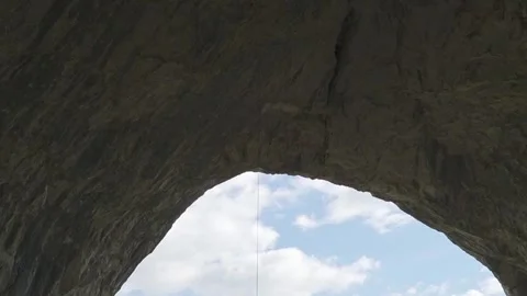 Camera Tilting Down tracking Climber Rappelling from Giant Rock Arch Stock Footage 345632454