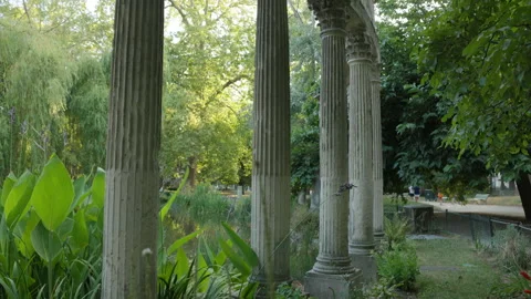 Camera Tilting Up View of Classical Stone Columns along a Lush Park Path and Pon Stock Footage 340477180