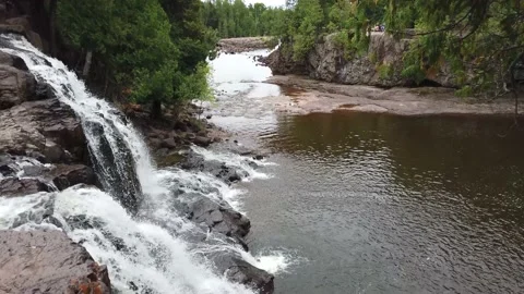 Camera tilts down rushing waterfall and focuses on water rushing into river. Stock Footage 157768135