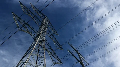 Camera tilts up to high voltage overhead power transmission lines with blue sky. Stock Footage