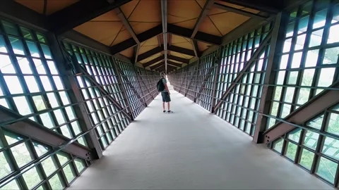 Camera Tracking Backpacker in Symmetrical Enclosed Pedestrian Bridge 스톡 동영상 333918026