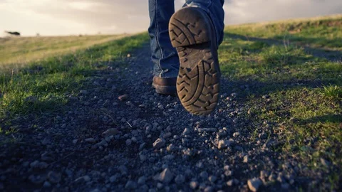 Camera tracking behind man in blue jeans and boots walking down a country road. Stock Footage 87856453