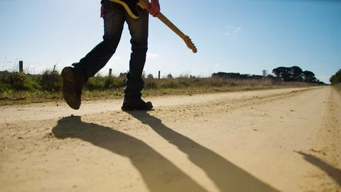 Camera tracking behind musician walking dusty road with guitar. Stock Footage 87839801