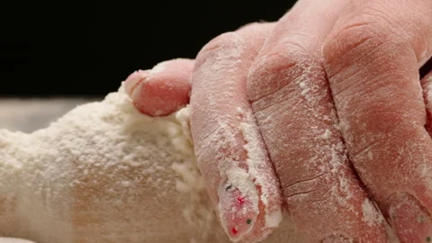 Camera tracking a hand sliding over a flour-dusted rolling pin as flour falls. 動画素材 323508603