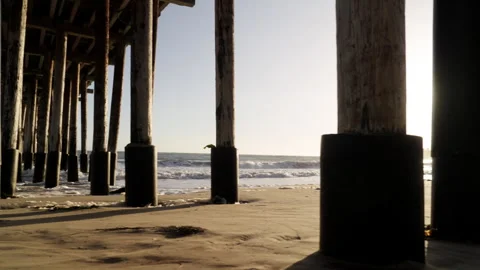 Camera tracking under pier at sunset looking out to waves Stock Footage 284805586