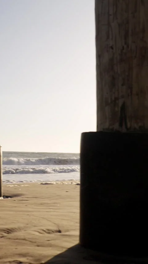 Camera tracking under pier at sunset looking out to waves vertical video Stockbeeldmateriaal 284811215