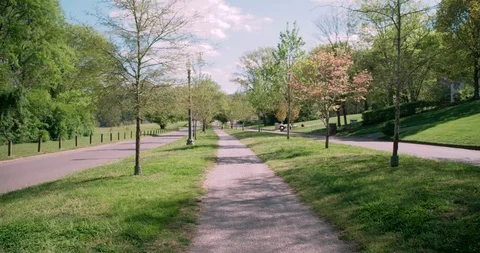 Camera tracks down shaded running path with cloudy skys Stock Footage