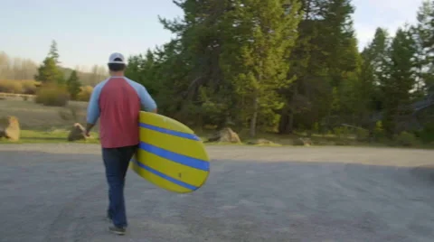 Camera tracks guy holding surf board Stock Footage 63385913
