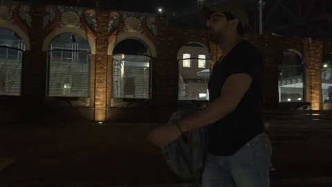Camera Tracks With Man, following as He Walks in Dimly Lit Urban Street Stockbeeldmateriaal 107899349