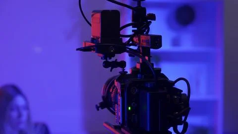 Camera on a tripod against a blurred background of a female presenter in a dark Stock Photos