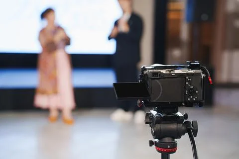 Camera on tripod capturing presentation at indoor event Stock Photos