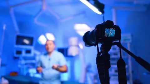 Camera on tripod set in modern surgery room. Unrecognized male doctor in blue Stock Footage 334339458