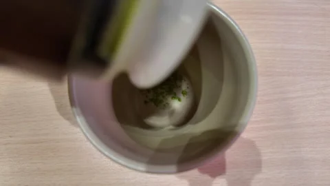 Camera video of matcha green tea powder being added to cup Stock Footage 325648920