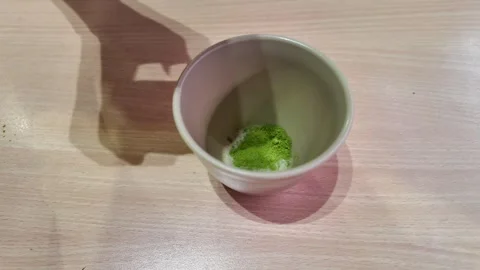 Camera video of matcha green tea powder being added to cup Stock Footage 325648930