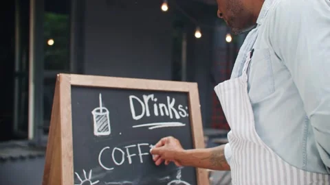 Camera view of African American man standing near cafe board and writing menu Stock Footage 254685763