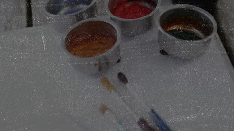 Camera view shifting downward revealing paint cups next to colored brushes Stock Footage 314528166