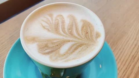 Camera zoom in on a mug of coffee on a blue saucer. Coffee Latte Art on milk Vídeos de archivo 151744185