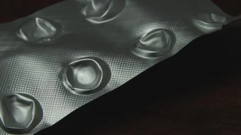The camera zooms in on an empty pill blister pack lying on a wooden surface.. Video stock 340902328