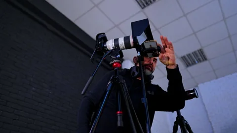 Cameraman adjusting camera lens and phone setup in studio. Low angle shot of man Video stock 334813164