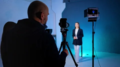 Cameraman stands backstage in modern studio. Cameras and soffits are directed on Vídeo Stock 329704571