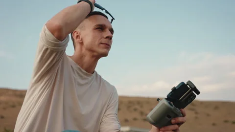 A cameraman in sunglasses holding a drone controller and watch drone fly Stock Footage 252673079
