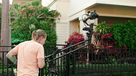 A cameraman is using a camera mounted on a crane to film outdoors, with a Stock Footage 241826686