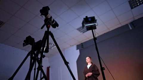 Cameras on tripods and soffits are directed on the woman talking and gesturing. Vídeo Stock 329704652