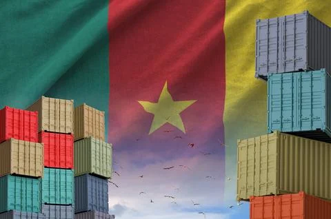 Cameroon flag and big stack of shipping cargo containers in docks with sky Stock Photos