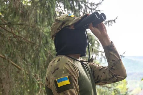 Camouflaged soldier scanning distant landscape with binoculars in forest 写真素材