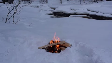 A camp fire is burning in the snow close to a river in blue hour of winter day Stock Footage 170884186
