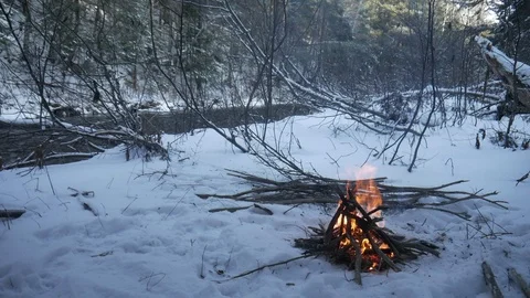 Camp fire in wilderness during winter with snow and stream in background Stock-Footage 121220465