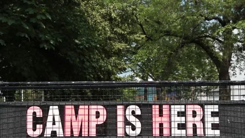 Camp is here sign with trees in background, colorful capital letters on black Stock Footage 247143966