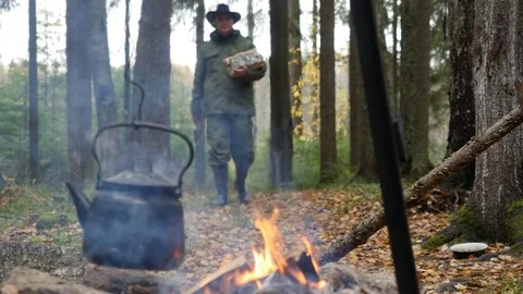 Camp kettle over burning fire and a hiker with firewood goes in background Видео 81427131