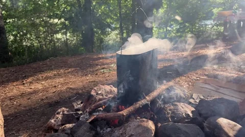 Camp kettle steams above stone campfire pit during camping in forest. Soot Vidéo 346724533
