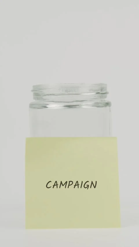 Campaign text or word on yellow sticky note attached to glass jar with hand Stock Footage 311685790