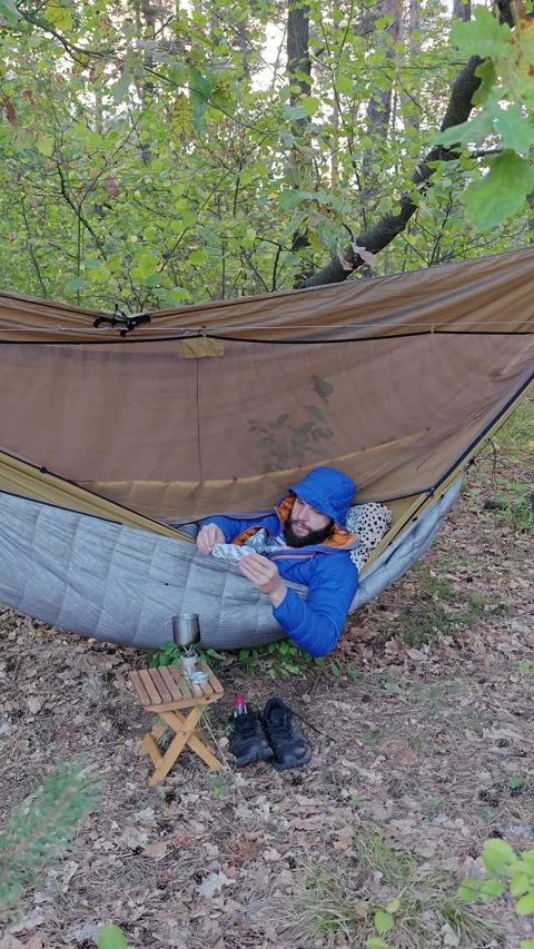Camper Covering Camp Mug With Foil Lid While Resting In Hammock 스톡 동영상 346550374